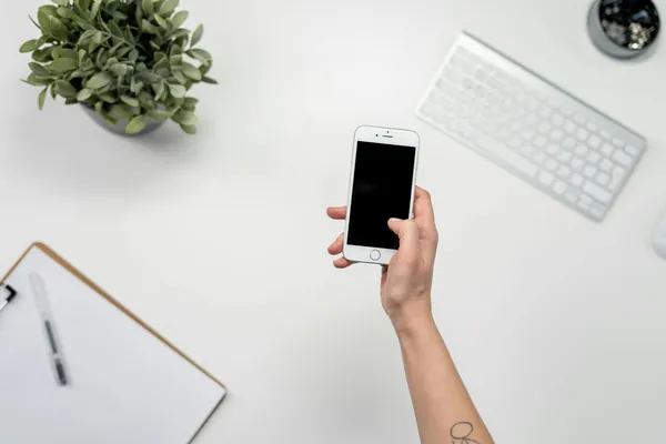 Mano sosteniendo un smartphone sobre un escritorio blanco