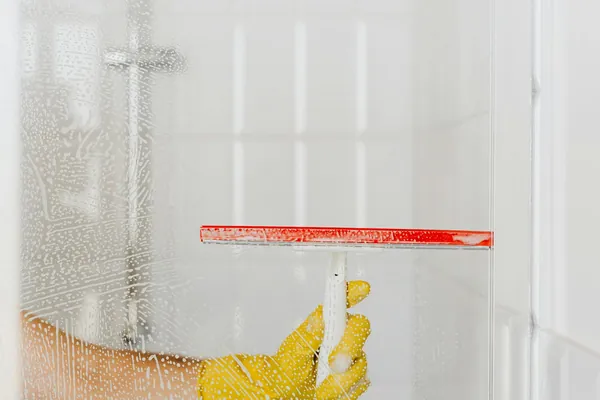 Persona limpiando el cristal de la ducha con rasqueta y guante