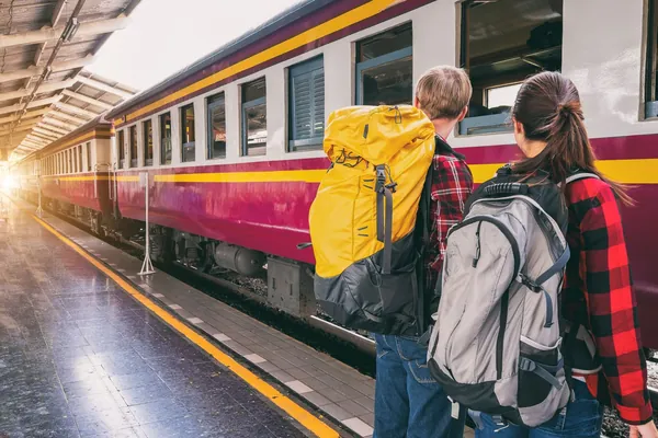 Viajeros con mochila en andén junto a un tren de pasajeros